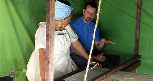 A director and cast member standing at a loom with a green screen behind